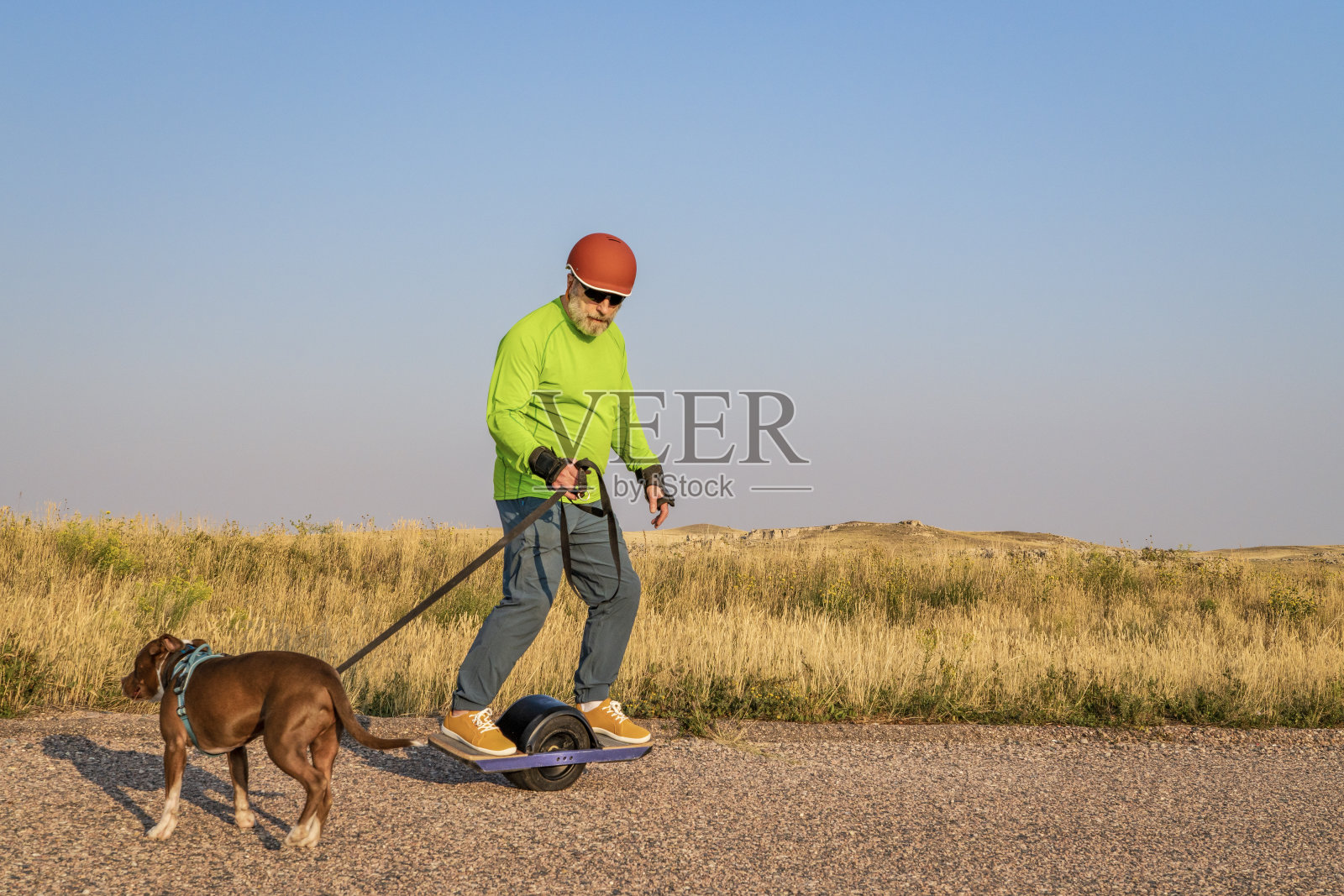 一名成熟的老年男子和一只狗一起骑着单轮电动滑板照片摄影图片