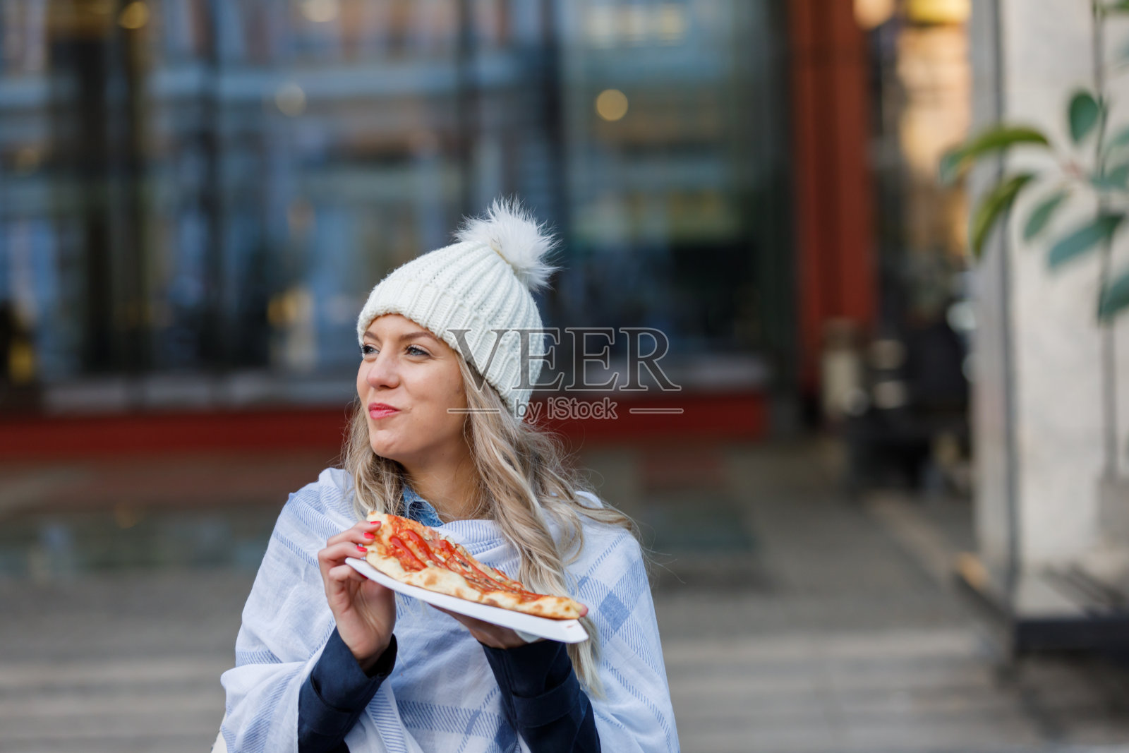 一个年轻的女人在街上一边走一边吃披萨。照片摄影图片