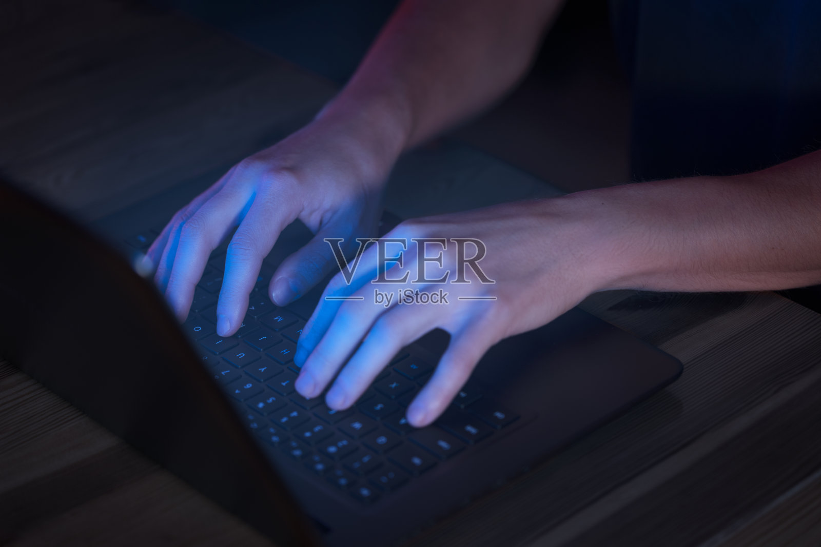 一名男子在黑暗中使用笔记本电脑，屏幕发出蓝色的光芒照片摄影图片