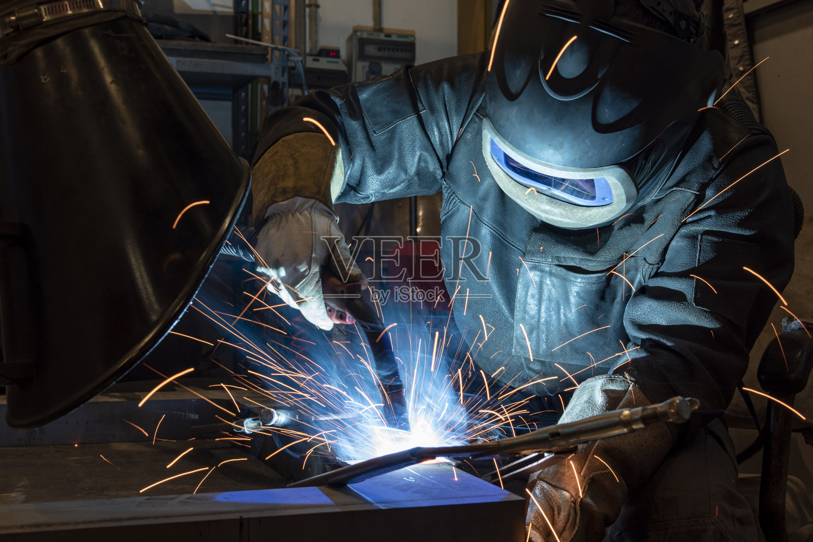 工厂的工业钢焊机。焊工用保护面罩焊接金属和火花照片摄影图片