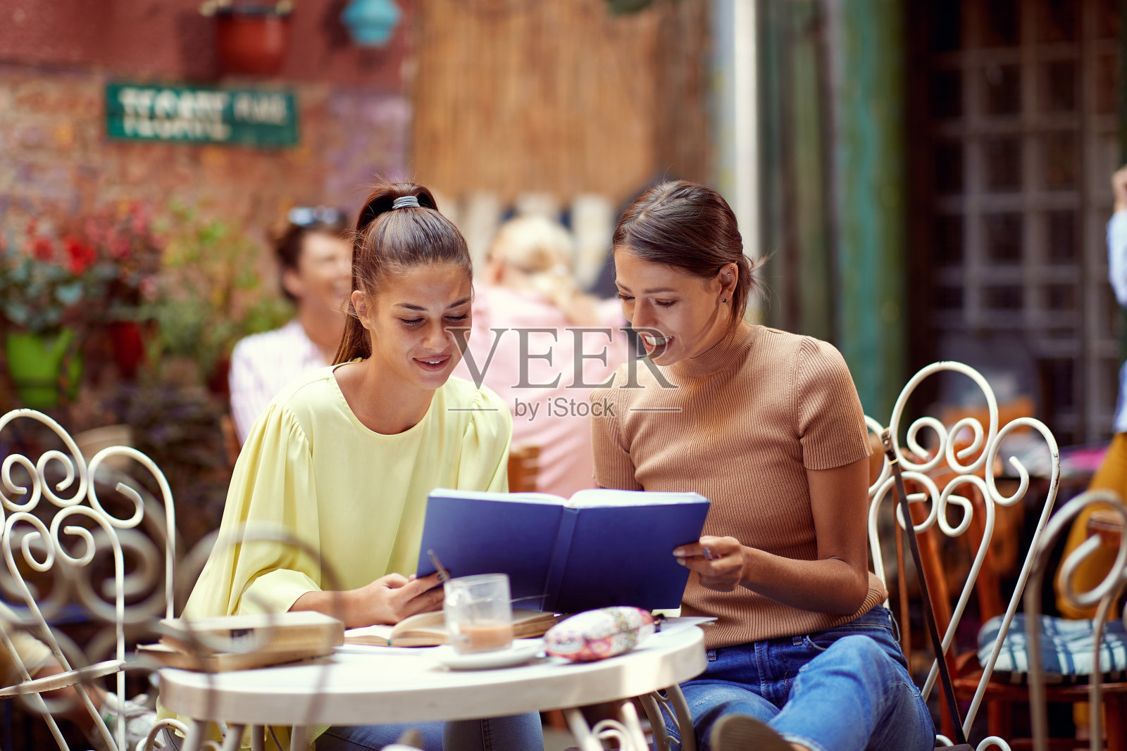 年轻的成年白人女性一起阅读笔记本，微笑，在户外咖啡馆照片摄影图片