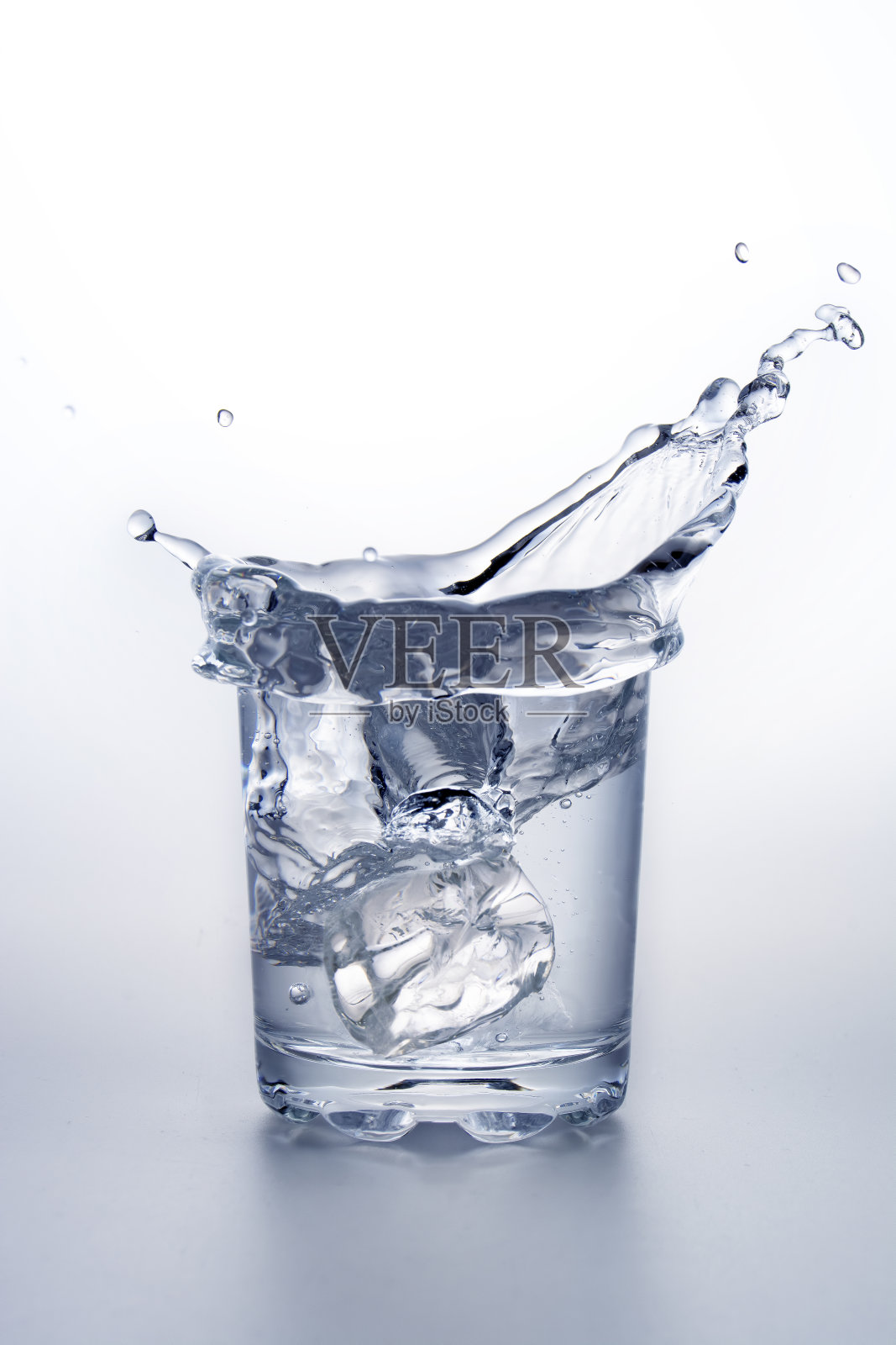 一杯溅着冰块的水。照片摄影图片