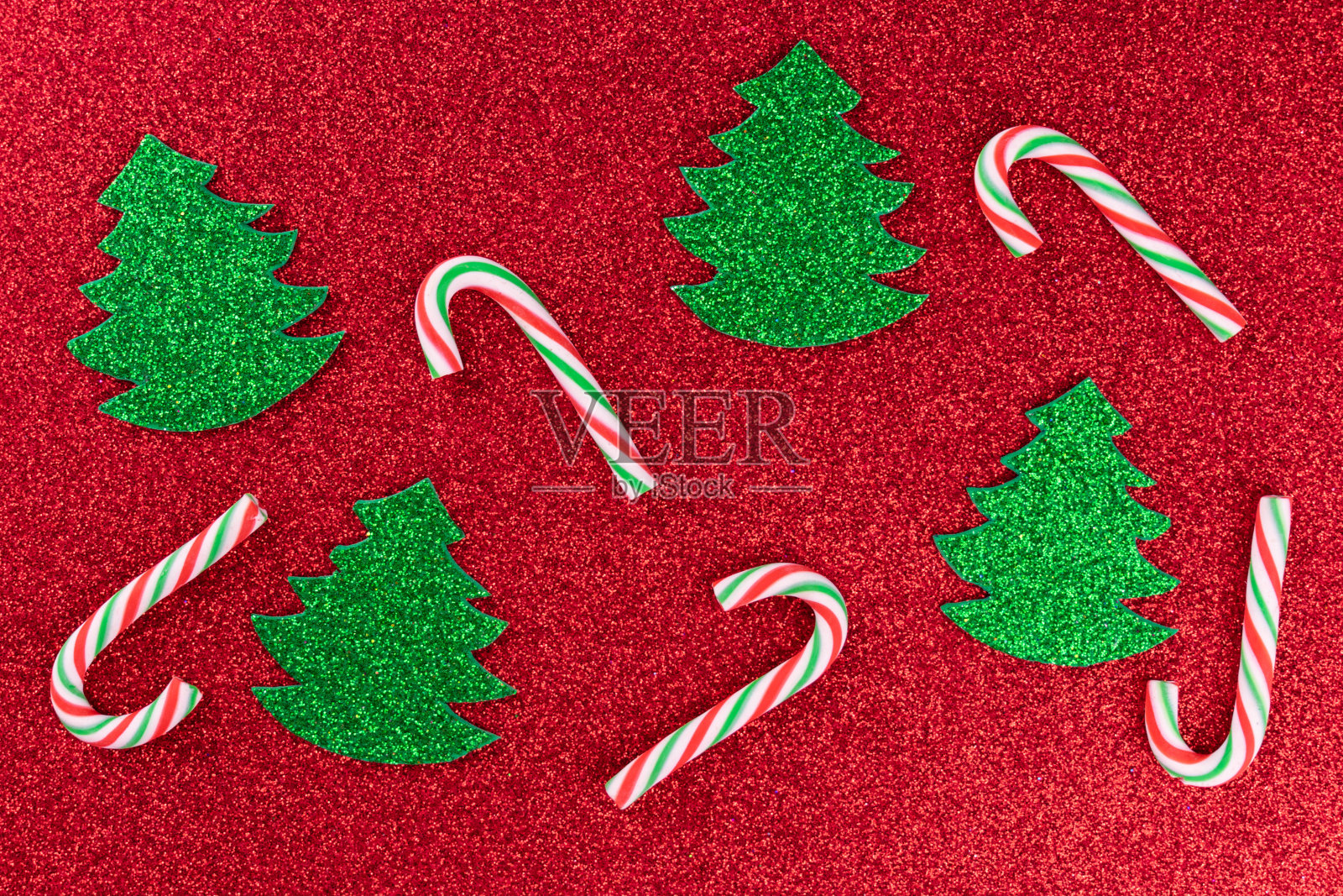 绿色的小圣诞树和红色背景上的条纹棒棒糖。照片摄影图片