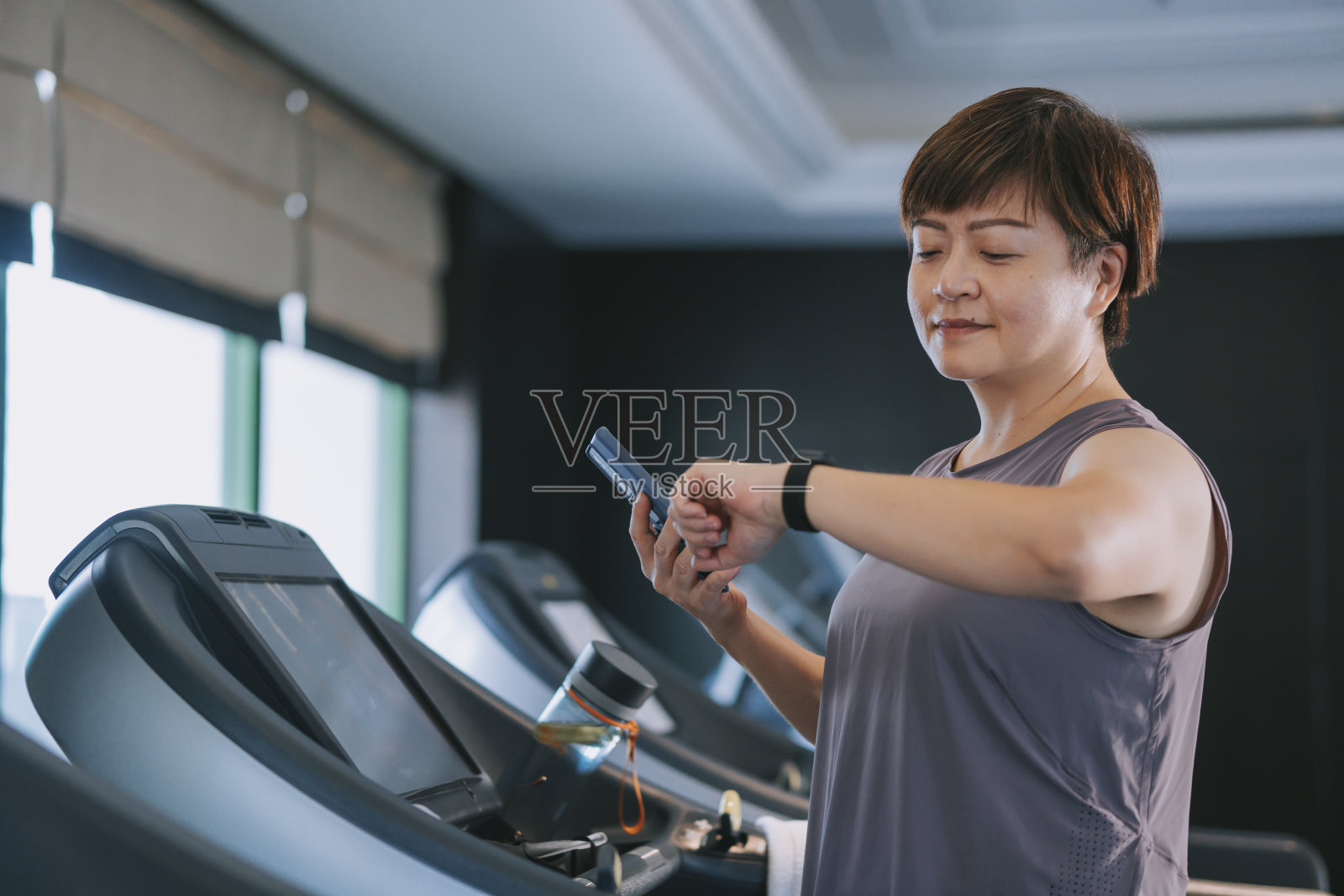 亚洲华人中年妇女运动后在健身房跑步机上用健身追踪器智能手表检查心率照片摄影图片
