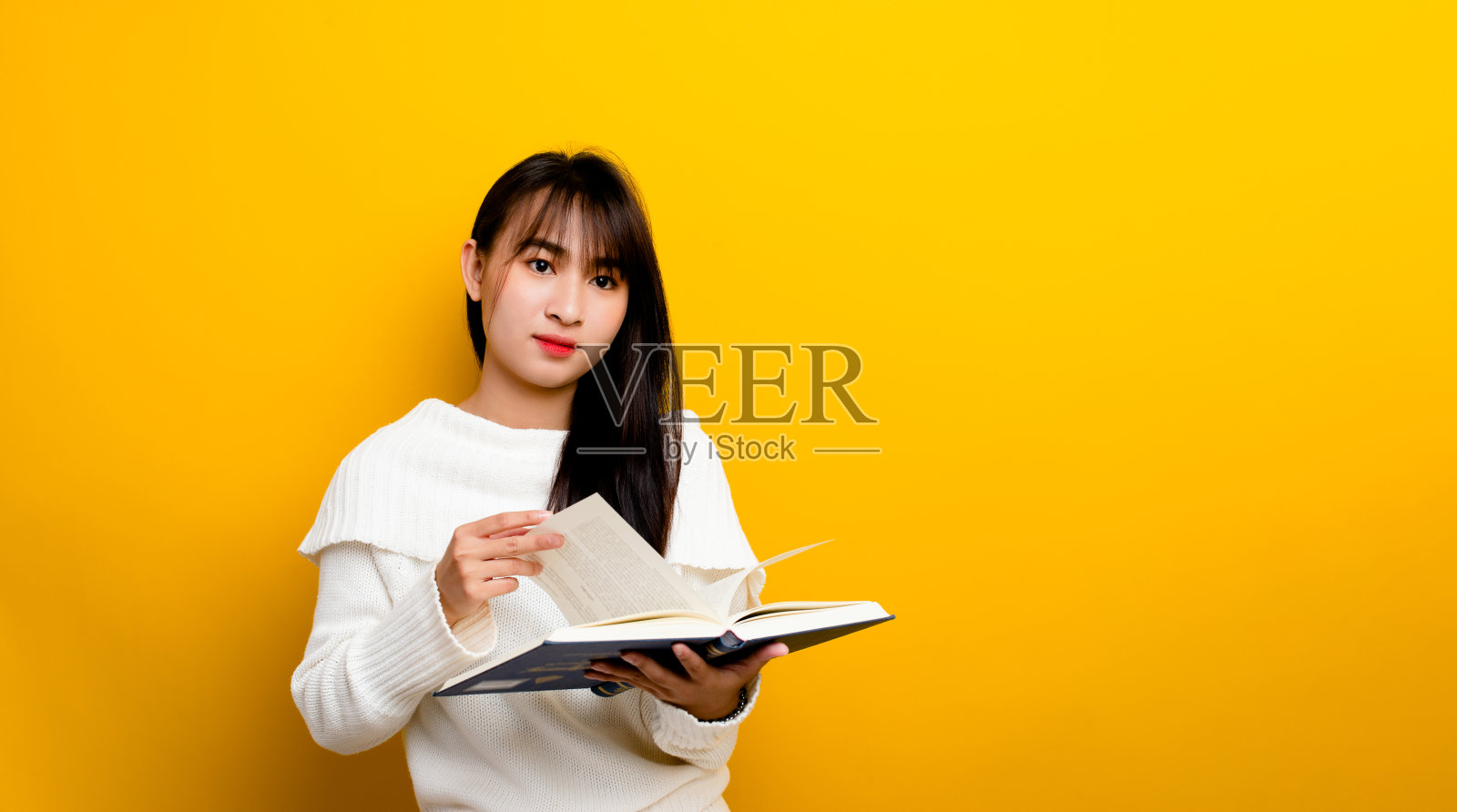 一个年轻的女人读一本书，然后像看电影一样思考。在黄色背景上照片摄影图片