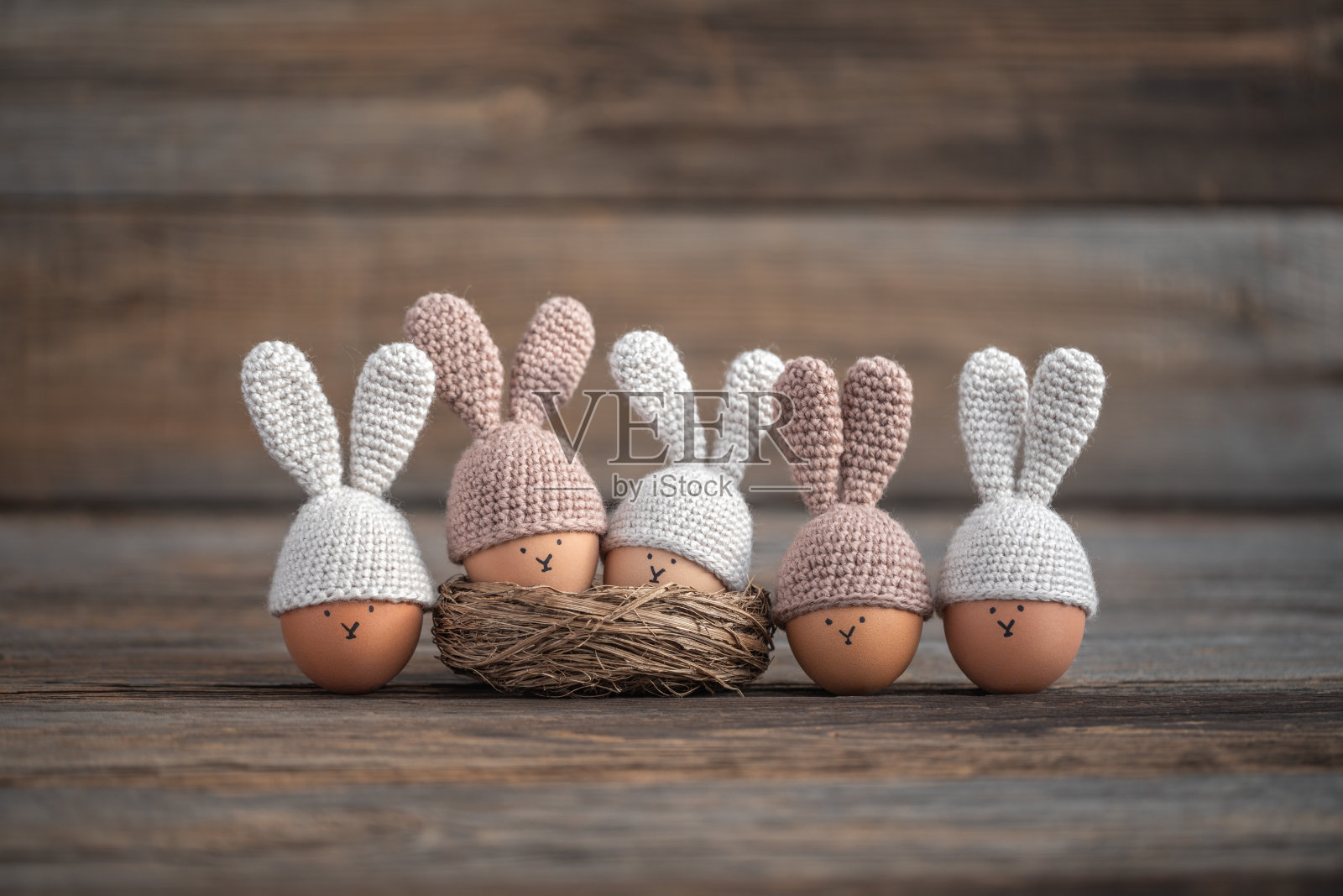 在一张质朴的木桌上，五个复活节彩蛋戴着兔耳朵钩编帽子。软的焦点。照片摄影图片
