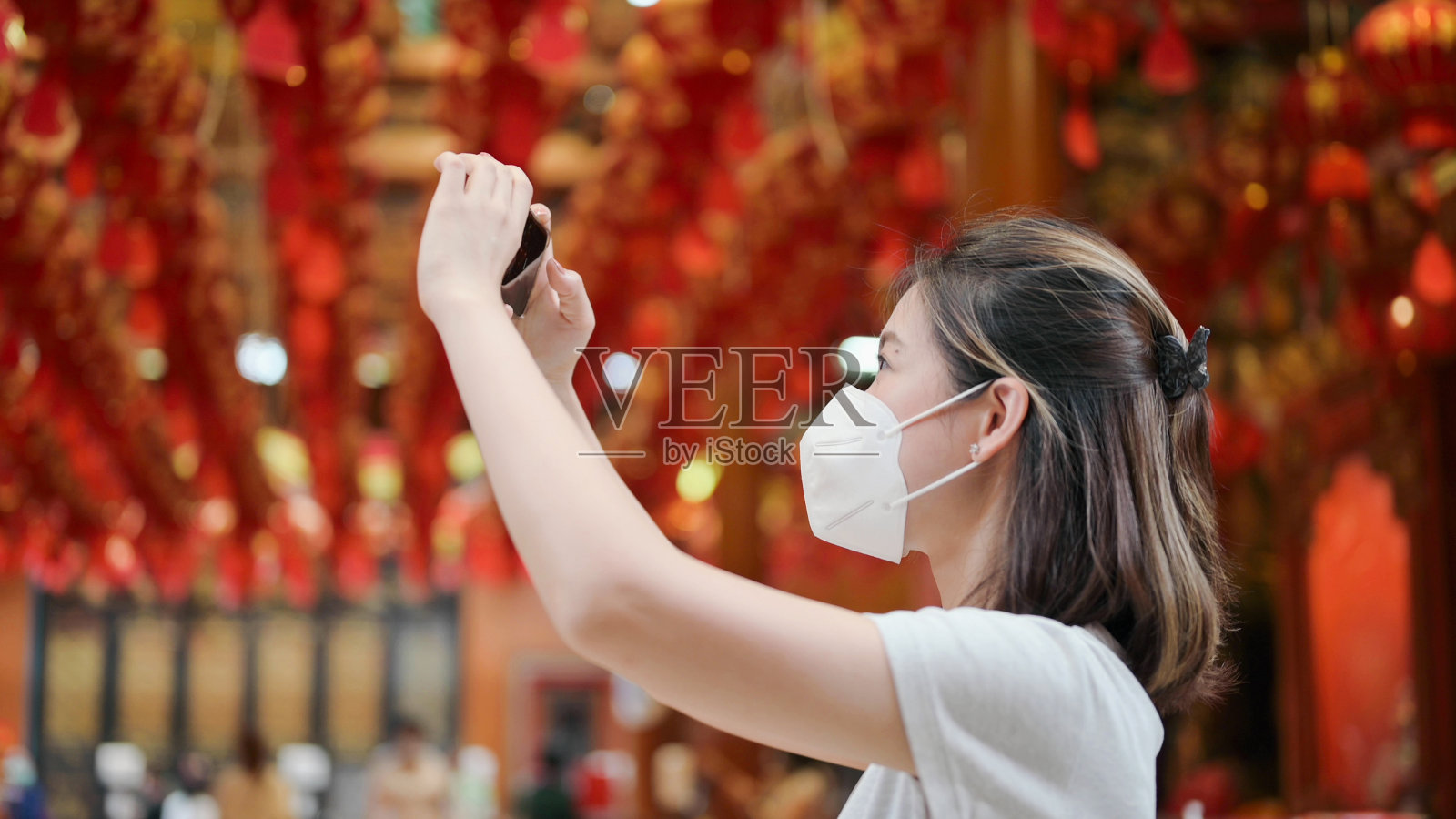 年轻微笑的女人戴着面具祈祷和使用手机记录Vlog红灯笼在曼谷唐人街冷内义寺泰国照片摄影图片