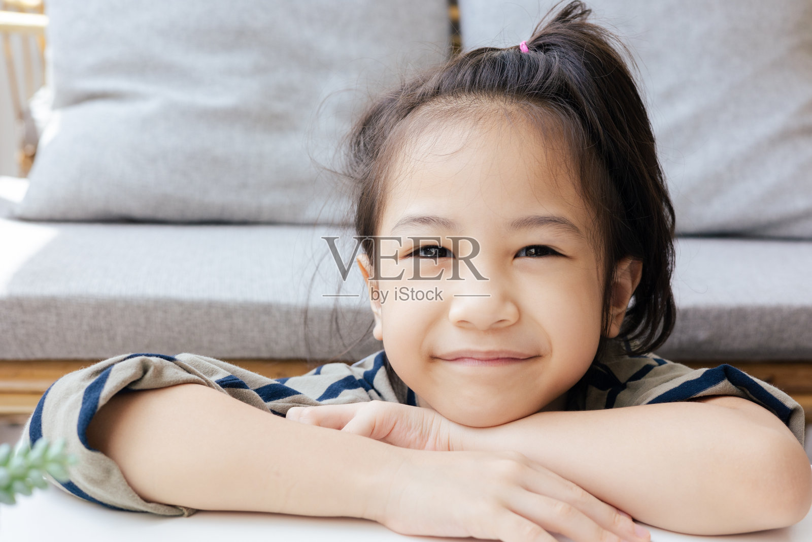 可爱的亚洲女孩在家里舒适的客厅里的脸特写，微笑着看着镜头，用美丽的阳光展现孩子的积极情绪、快乐、幸福。照片摄影图片