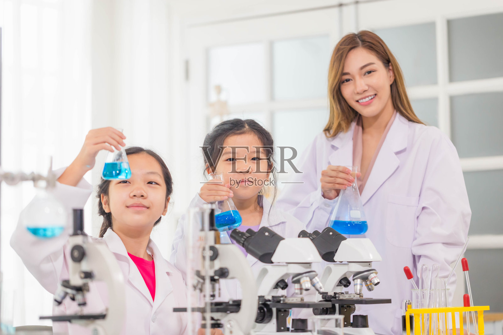小学科学课上，活泼的小朋友和科学老师一起在学校实验室展示装有化学液体的测试瓶，科学实验室照片摄影图片