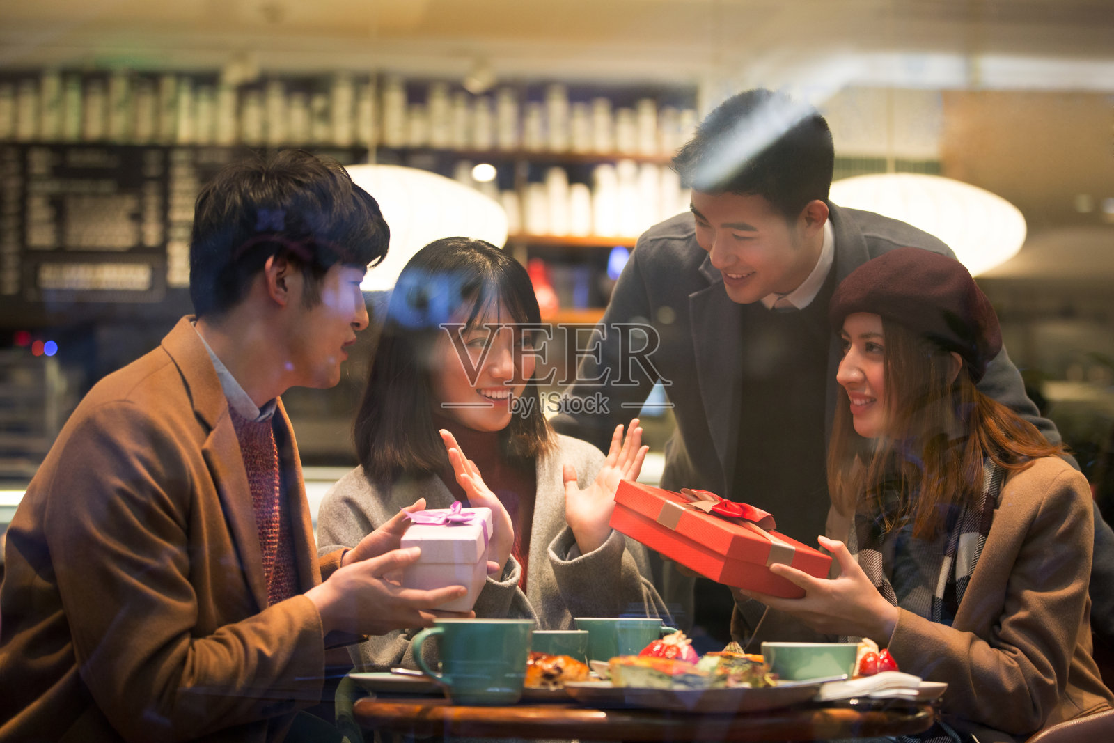 在冬天，年轻的东亚人坐在餐厅里，给朋友送惊喜礼物照片摄影图片