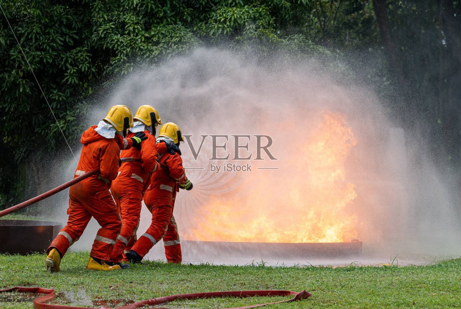 消防队员使用灭火器和高压水喷从软管控制火灾。模拟油气火灾事故中消防队员控制火势不扩散的训练。照片摄影图片