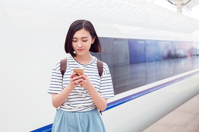 一名女子在火车站站台上用智能手机等待图片下载